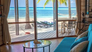 Una habitación con un gran ventanal con vista a una playa, una terraza de madera y un sofá azul.