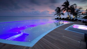 Una piscina con muelle de madera, palmeras y vista al atardecer.