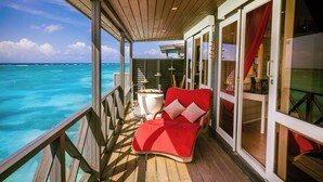 Una terraza de madera con un sofá rojo y una mesita pequeña, con vista a aguas turquesas.