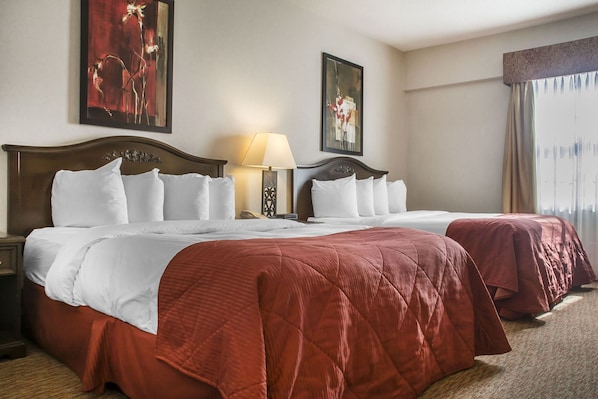 Habitación de hotel con dos camas, una mesita de noche, una lámpara y obras de arte en las paredes.