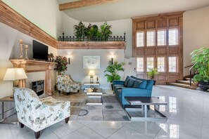 Amplia sala de estar con chimenea, televisor y diferentes opciones de asientos, incluyendo un sofá y sillones.
