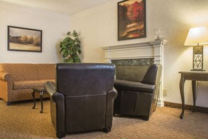 Una sala de estar con un sofá, dos sillones, una chimenea, una lámpara y dos cuadros enmarcados en la pared.
