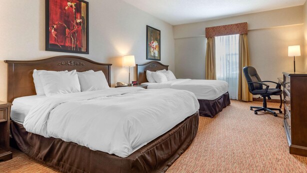 A hotel room with two beds, a desk, a chair, and artwork on the walls. - Quality Inn Sarnia (Point Edward)