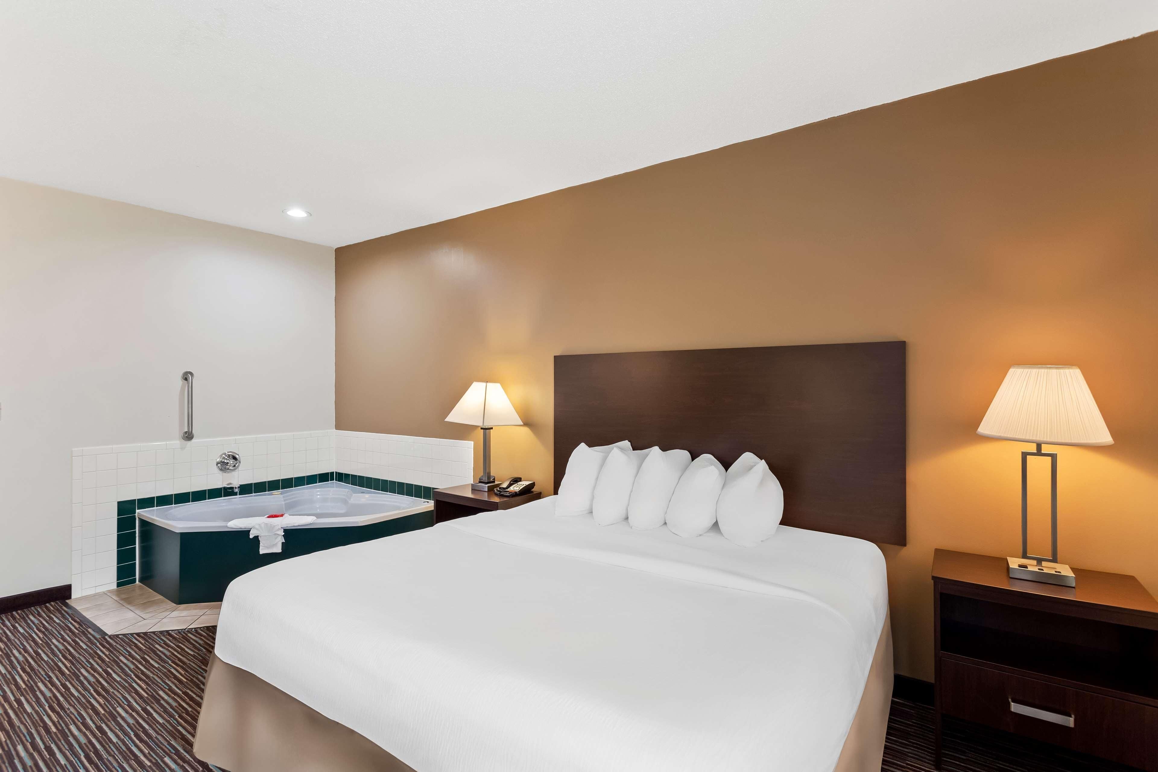 A hotel room with a large bed, a separate bathroom with a bathtub, two bedside lamps, and a nightstand with a phone.