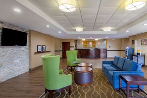 En hotellobby med gröna fåtöljer, en blå soffa, en platt-TV, en receptionsdisk och en mönstrad matta.