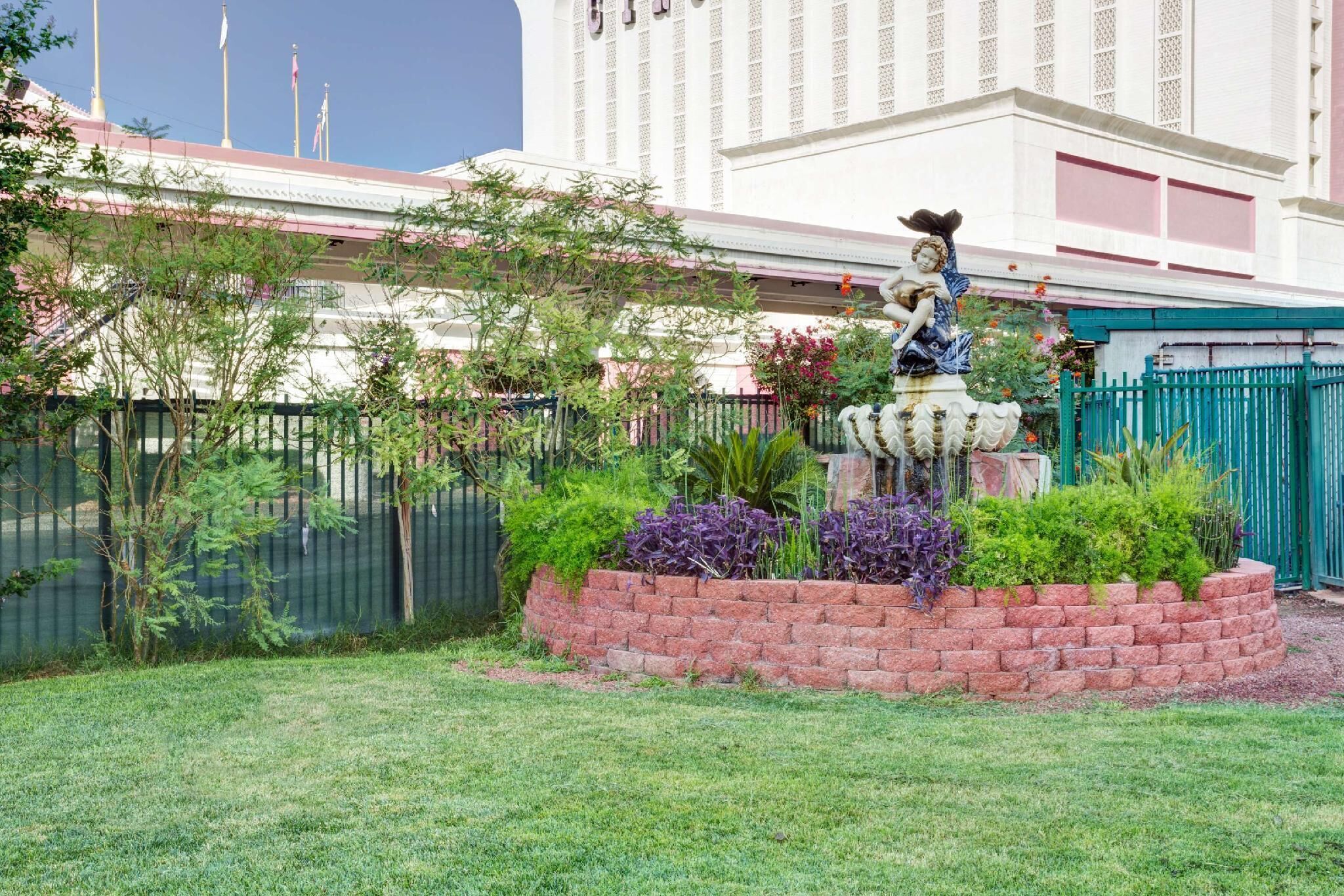 A building with a statue, a brick garden bed, and a green fence.