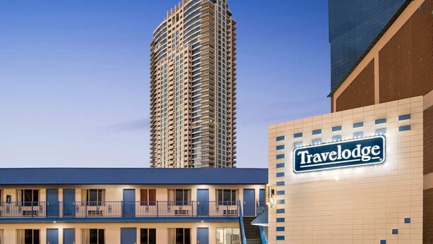 A Travelodge motel with a two-story structure, a prominent sign, and a tall building in the background.