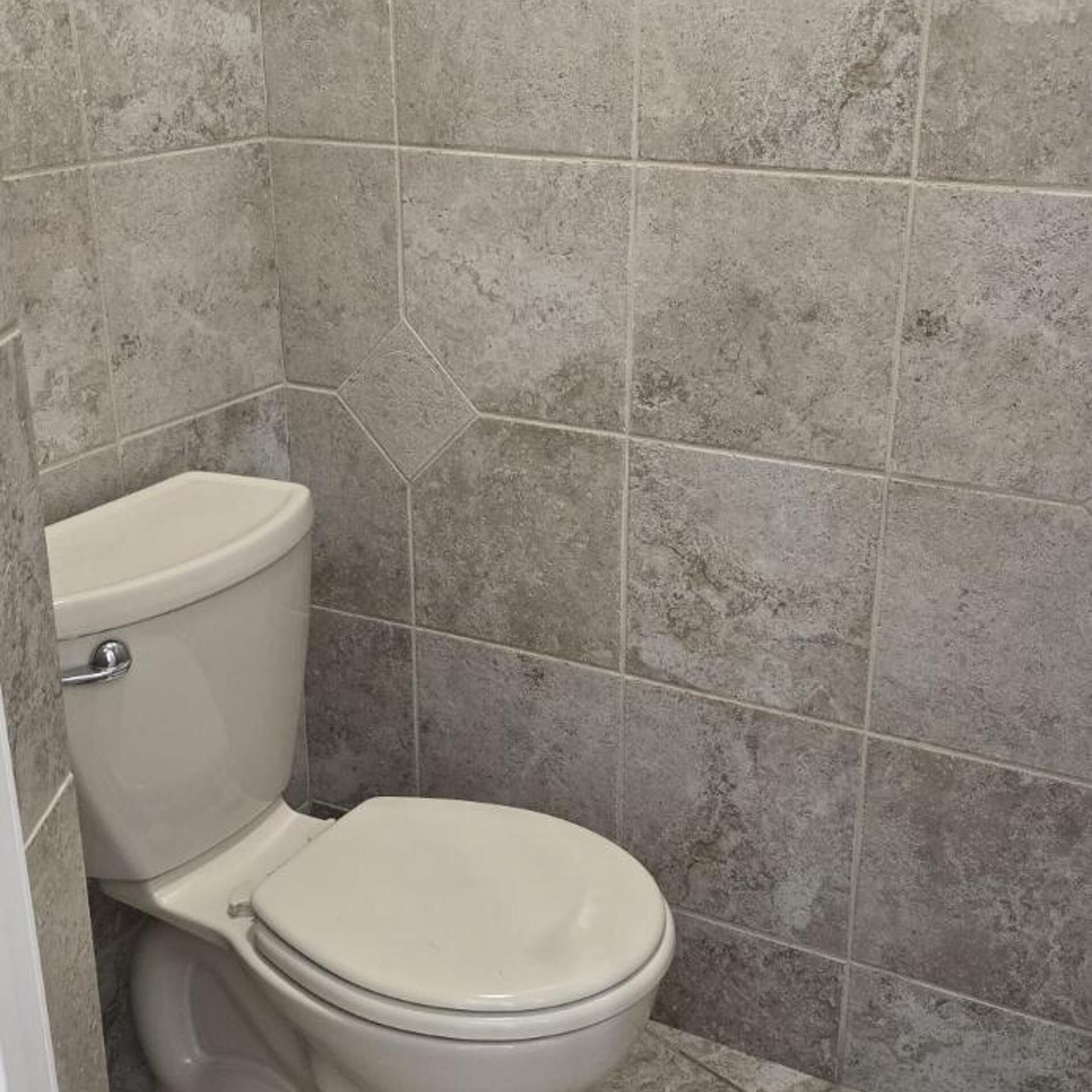 Une salle de bain avec des toilettes, des murs carrelés et une fissure visible dans le carrelage.