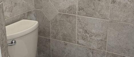 Une salle de bain avec des toilettes, des murs carrelés et une fissure visible dans le carrelage.