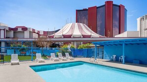 A swimming pool with lounge chairs, a covered area, and a building with a red and white facade.