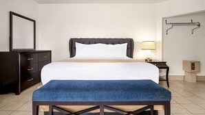 A hotel room with a bed, a bench, a dresser, a nightstand, a lamp, and a towel rack.