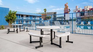 A poolside area with tables and chairs, a fenced pool, and a building with a blue facade.