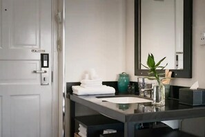 A modern bathroom with a white door, a black countertop, a sink, a mirror, and a vase with a plant. - C Central Hotel de Tham (Ho Chi Minh City)