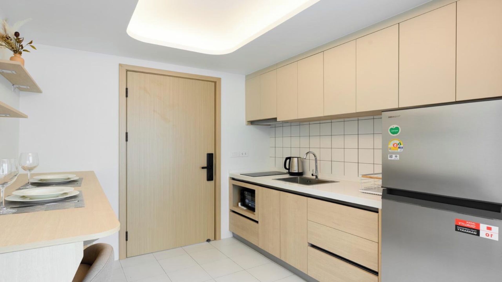 Une cuisine moderne avec des meubles en bois, un réfrigérateur en acier inoxydable et un coin repas avec une table dressée pour deux personnes.