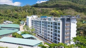 Ein mehrstöckiges Hotel mit modernem Design, umgeben von üppiger Vegetation und Hügeln.
