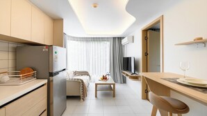 Eine kleine Küche mit Kühlschrank, einem Esstisch mit Stühlen, einem Fernseher und einem Fenster mit Vorhängen.