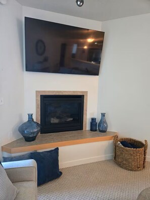 Una sala de estar con chimenea, un televisor montado en la pared y una cesta tejida en el suelo.