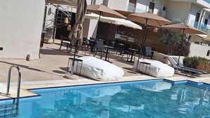 Piscina con sillas de descanso y sombrillas, rodeada por un edificio con área de estar al aire libre.
