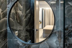 Et badeværelse med cirkulært spejl, marmorvægge, et badekar og et toilet.