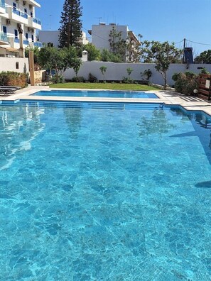 A clear swimming pool with a tiled deck, surrounded by greenery and buildings. - Soho Blue City Hotel (Hersonissos)