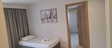 A hotel room with a bed, a painting on the wall, a door leading to another room, and a window with curtains.