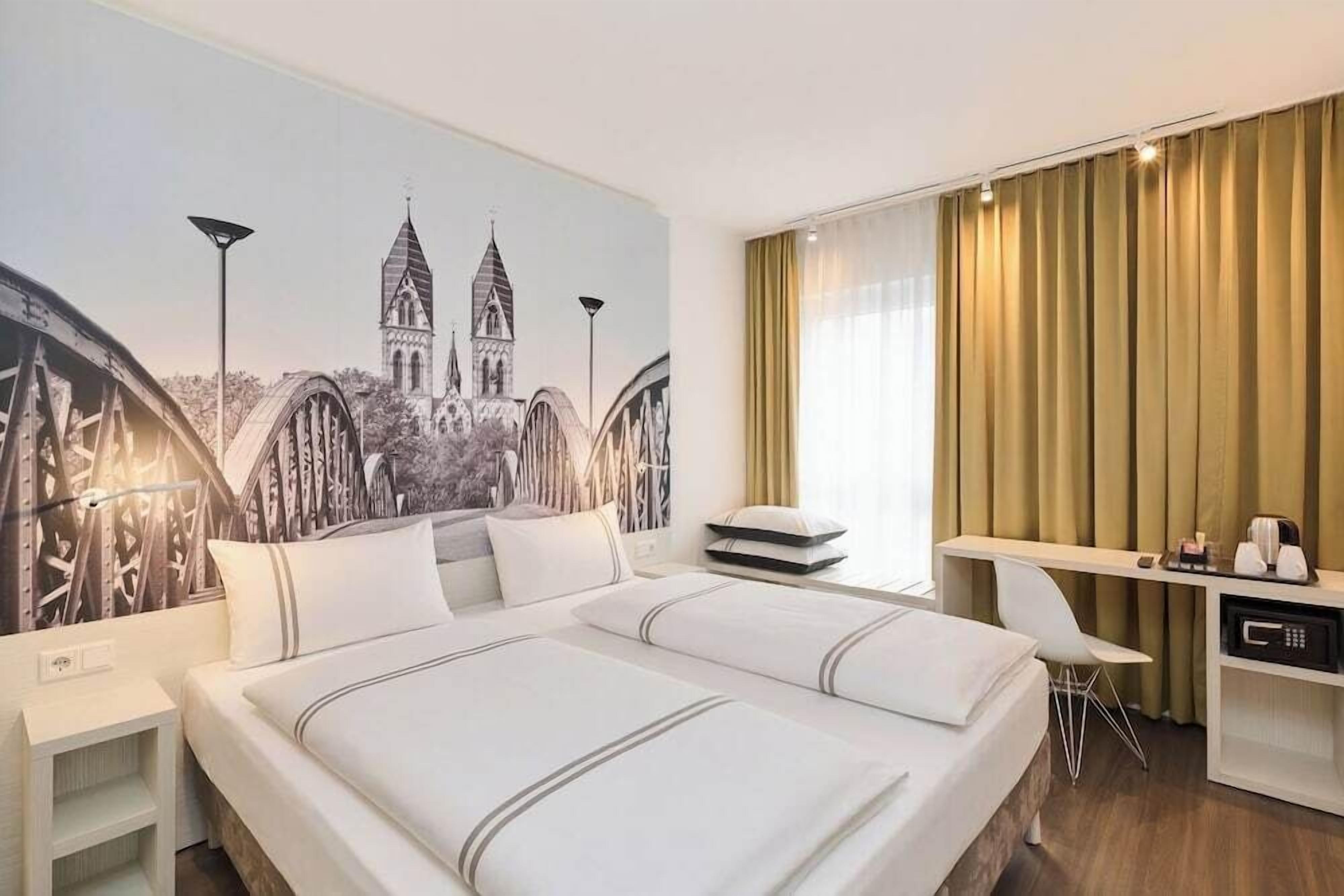 Une chambre d’hôtel avec un grand lit, un bureau, une chaise et une fresque murale.