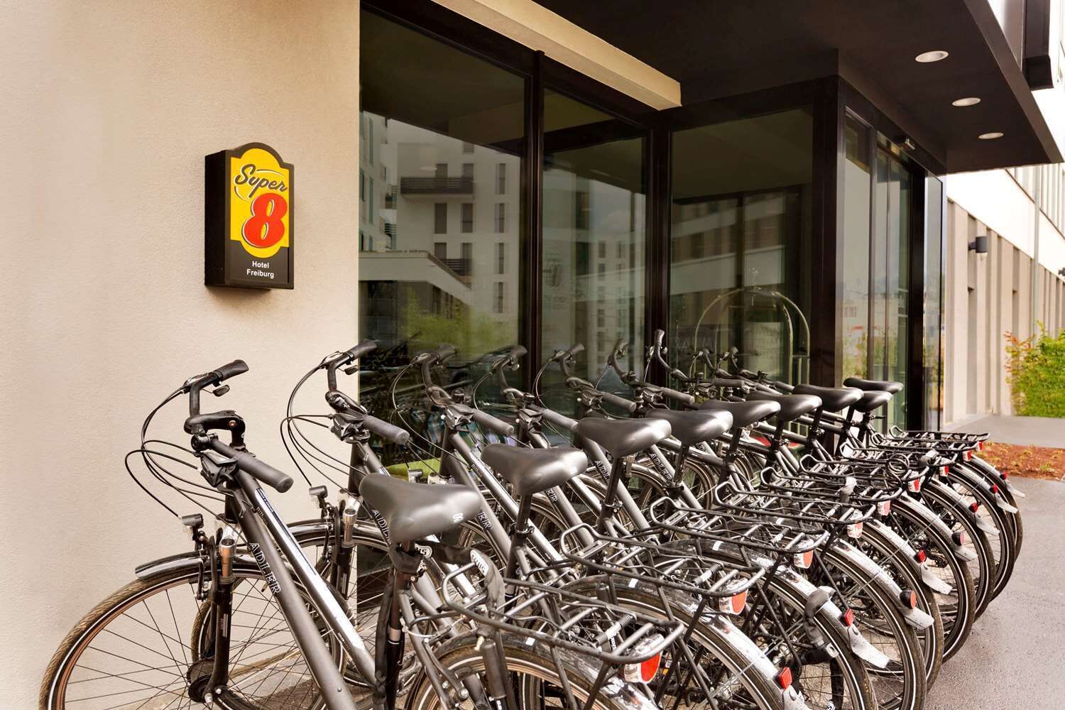 Eine Reihe von Fahrrädern, die vor einem Gebäude geparkt sind, an dem ein Schild mit der Aufschrift 'Super 8 Hotel Freiburg' hängt.