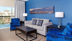 Ett hotellrum med en blå vägg, en grå soffa med mönster, en blå fåtölj, ett träbord och en tavla som föreställer en stadsbild.