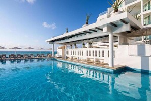 Un espace aménagé au bord de la piscine, avec des chaises longues et des parasols, un ciel dégagé et une vue sur la mer.
