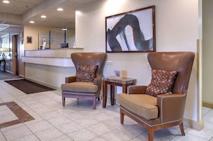 A lobby with two leather armchairs, a reception desk, and a large abstract painting.