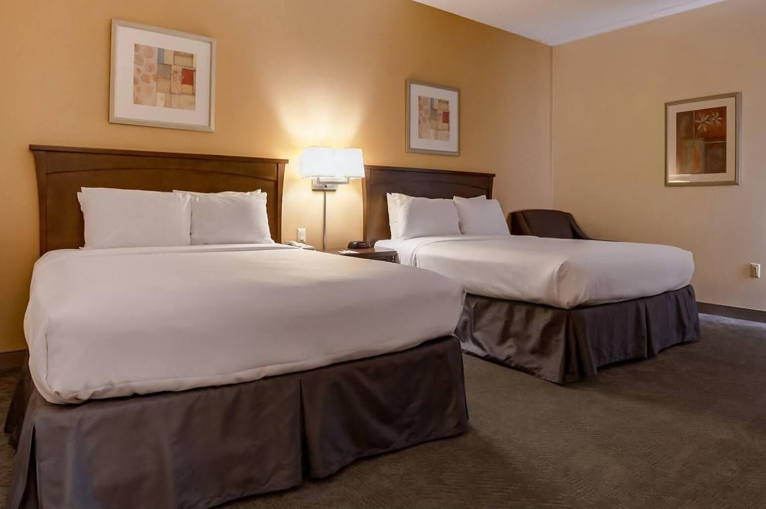 A hotel room with two beds, a nightstand, a lamp, and artwork on the walls.