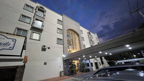Un hôtel à la façade moderne, doté de nombreuses fenêtres et dont l’entrée se trouve sous un pont.