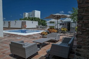 Un espace piscine aménagé sur le toit, avec des chaises longues, une table et des plantes en pot.