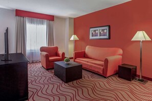 Habitación de hotel con pared roja, un sofá, una silla, una mesita de centro, un televisor y dos lámparas.