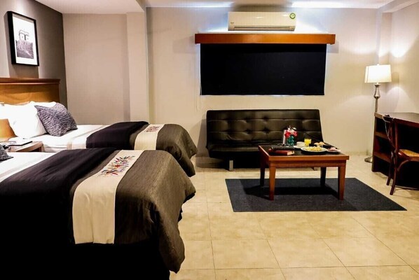 Habitació d'hotel amb dos llits, un sofà, una taula petita amb aliments per esmorzar, un aparell d'aire acondicionat i un televisor fixat a la paret.