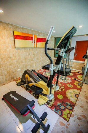 Un gimnasio en casa con equipo de ejercicio, incluyendo una cinta de correr, una bicicleta estática y un banco de pesas.