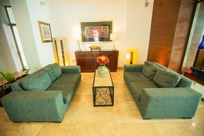 A living room with two green sofas, a coffee table with a vase, a wooden cabinet, and a painting on the wall. - Nacional Hotel Merida (Mérida)