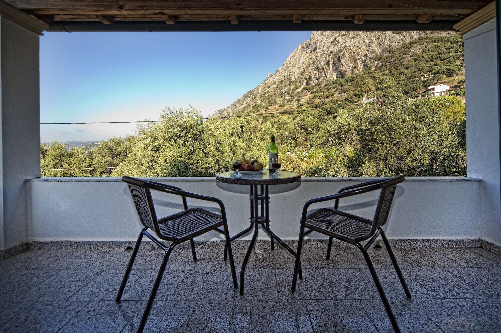 A balcony with two chairs and a table, a bottle of wine, and a bowl of fruit.