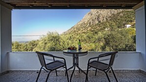 Un balcon avec deux chaises et une table, une bouteille de vin et un saladier de fruits.