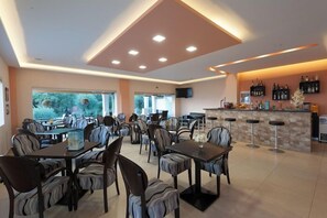 A restaurant with multiple tables and chairs, a bar area, and a television mounted on the wall. - Crystal Blue Aparthotel (Corfu)