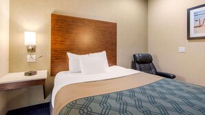 Une chambre d’hôtel comprenant un lit, un bureau, une chaise, une lampe fixée au mur et un tableau encadré.