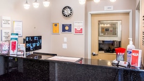 Un espace d’accueil d’hôtel comprenant un comptoir d’enregistrement, une horloge, des trophées encadrés et un panneau indiquant l’emplacement des bureaux.