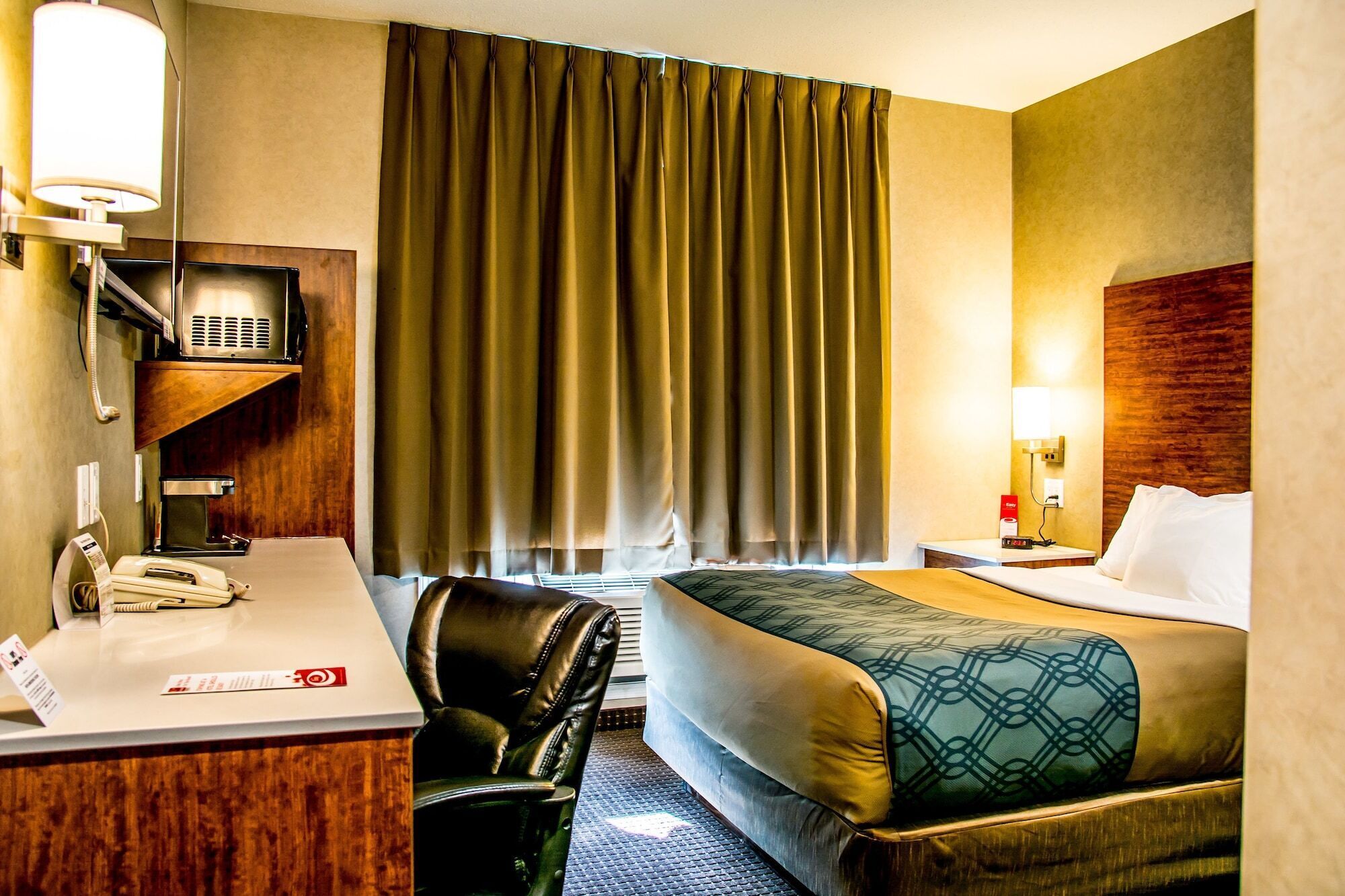 A hotel room with a bed, desk, chair, and a telephone.
