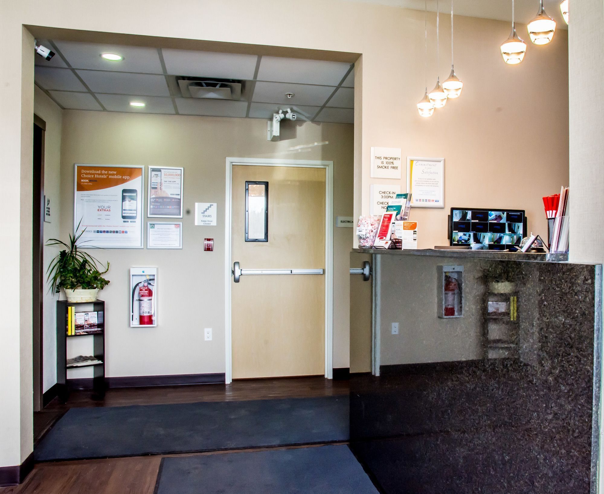 A hotel reception area with a reception desk, a plant, a fire extinguisher, and various informational posters on the wall.