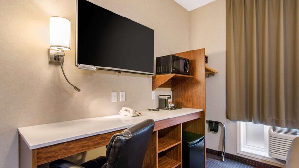 Une chambre d’hôtel équipée d’un téléviseur à écran plat, d’un bureau avec un téléphone, d’un four à micro-ondes, d’une poubelle et d’une chaise.