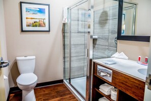 A modern bathroom with a toilet, glass shower enclosure, and a vanity with a mirror and towel rack. - Econo Lodge Fox Creek, AB (Fox Creek)