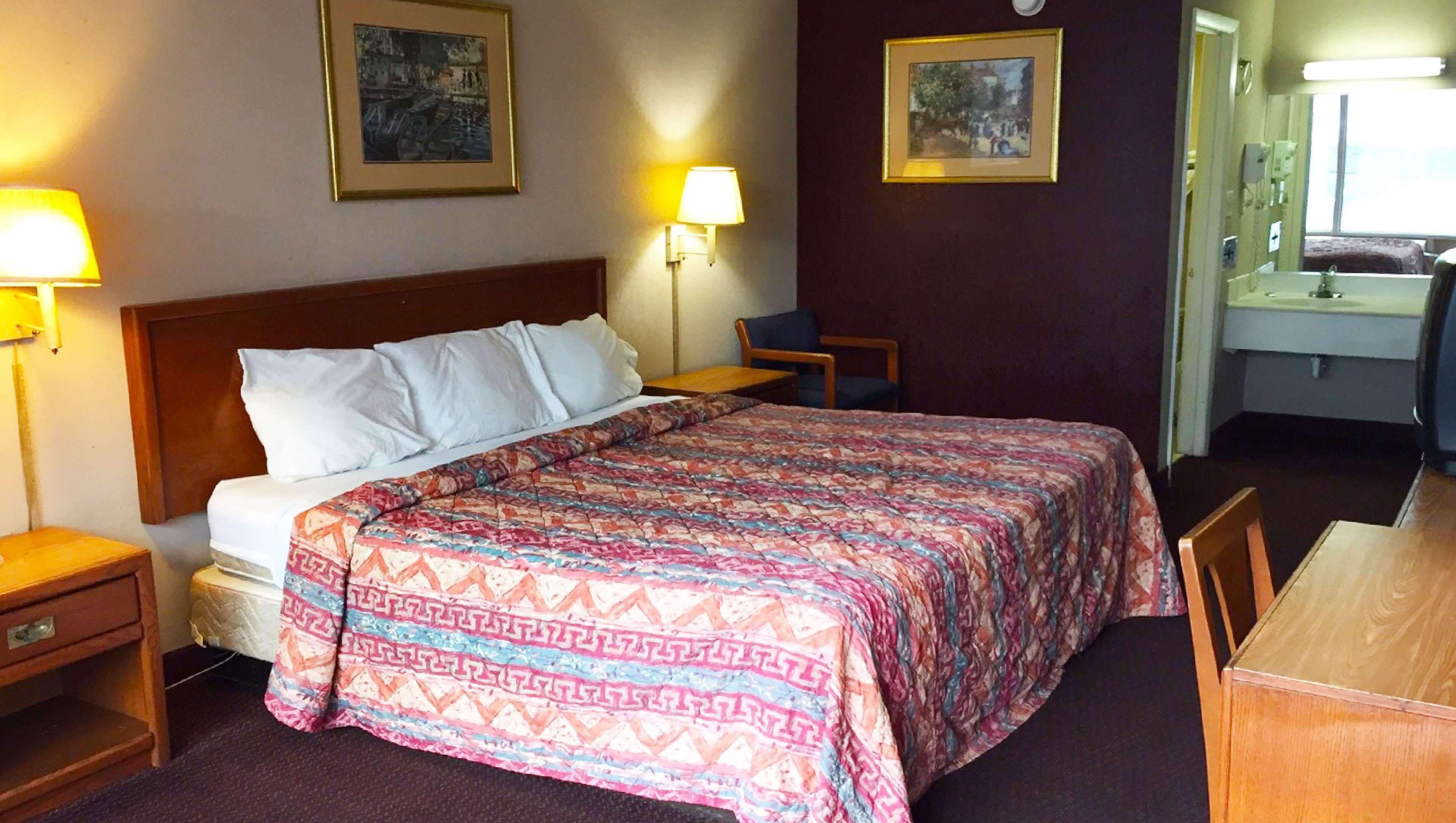 A hotel room with a bed, bedside tables, lamps, a desk, and a mirror.