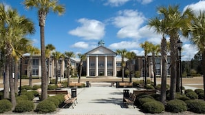 A building with a central entrance, flanked by palm trees and benches, under a clear sky. - Magnuson Hotel Columbia (Columbia)