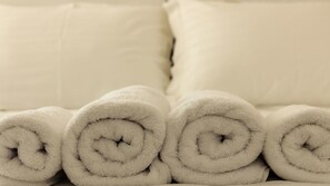 Una cama con toallas blancas enrolladas y almohadillas lisas.