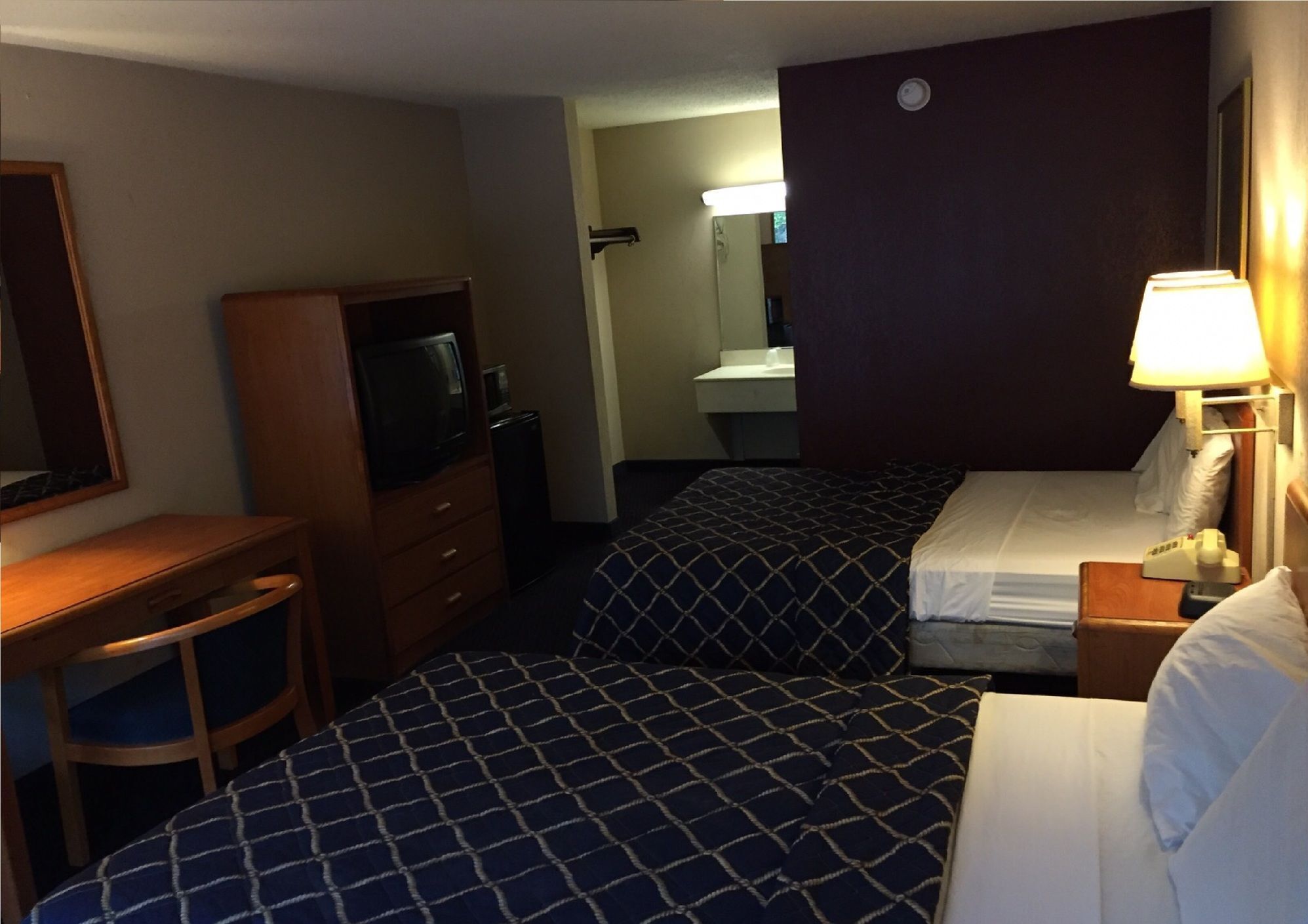 A hotel room with a bed, a desk, a television, a mirror, and a bathroom.